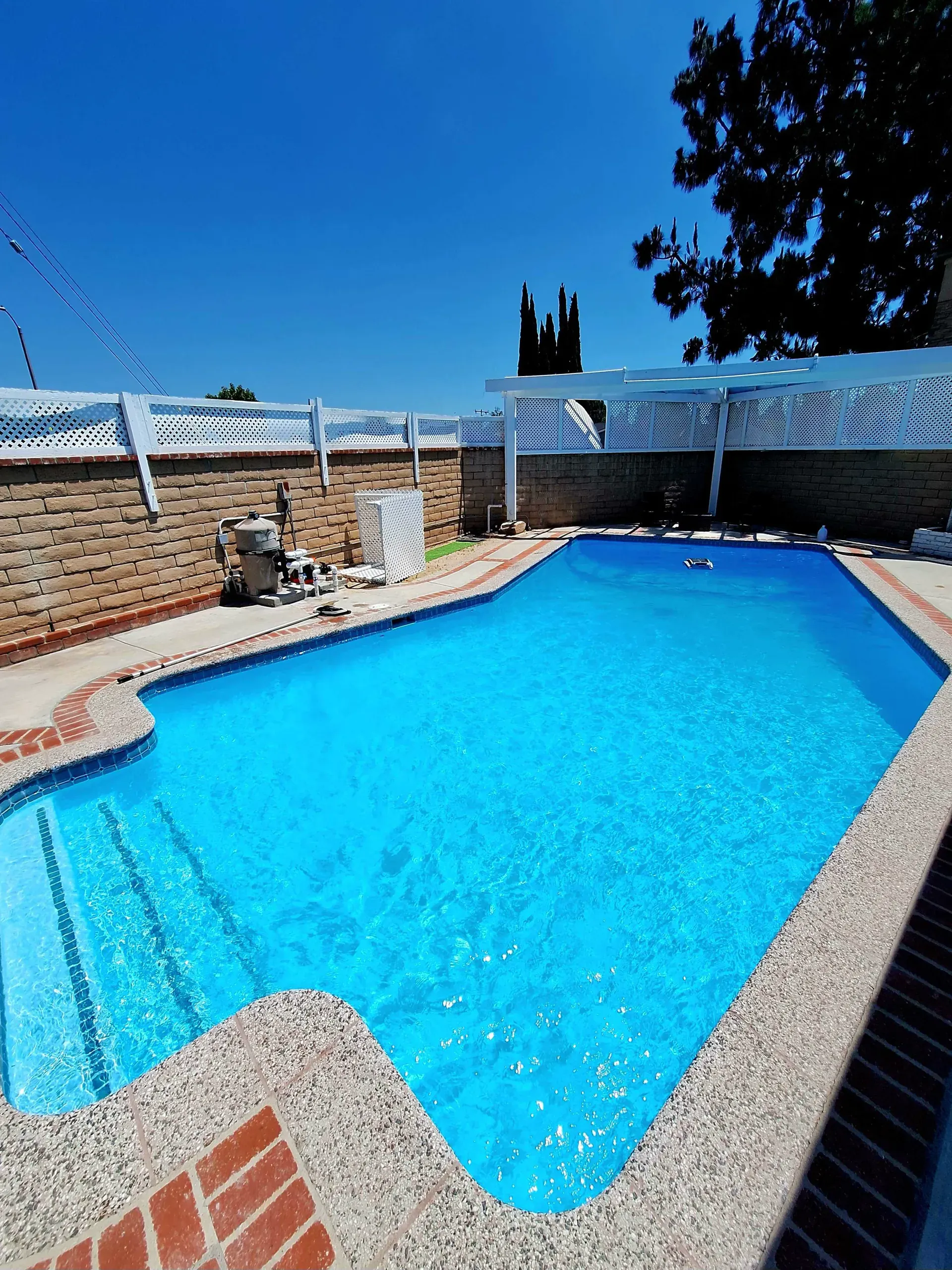 A bright blue backyard pool after cleaning, with the equipment pad visible along the far edge