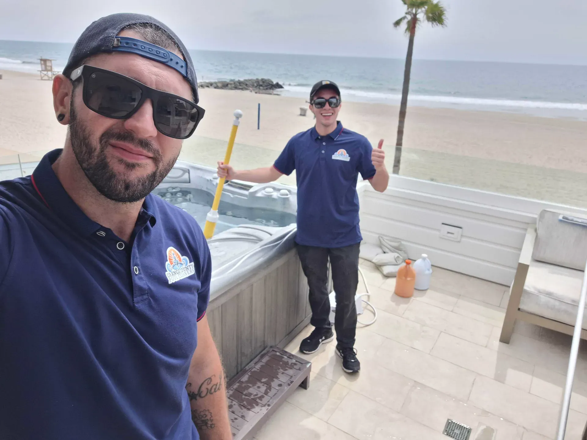 Two uniformed technicians standing beside a hot tub at an oceanfront job site