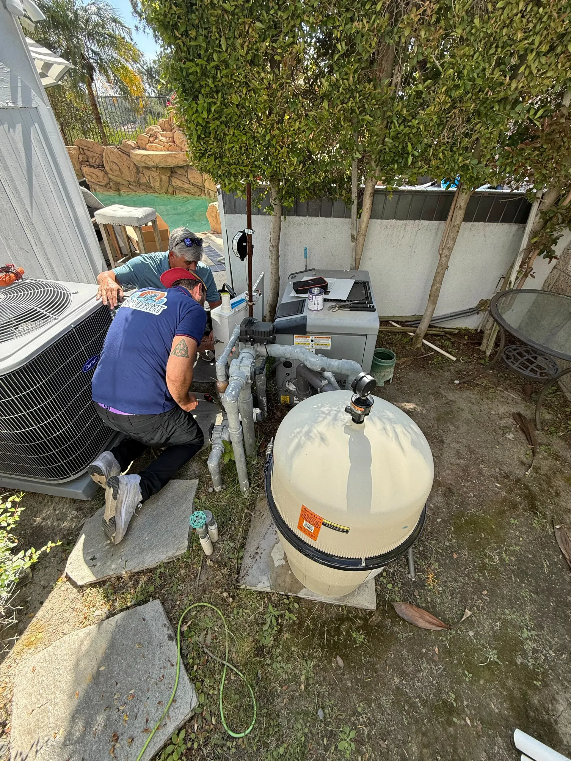 Two technicians working on a pool pump and filter equipment pad